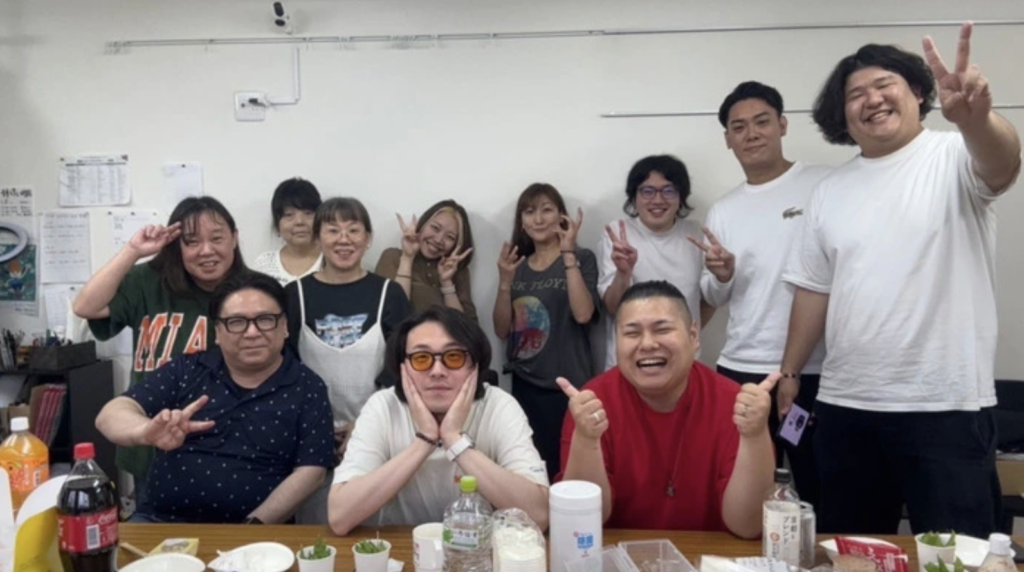 ケイズのスタッフの皆さんと利用者の方がカメラに向かって大人数でピースしている。